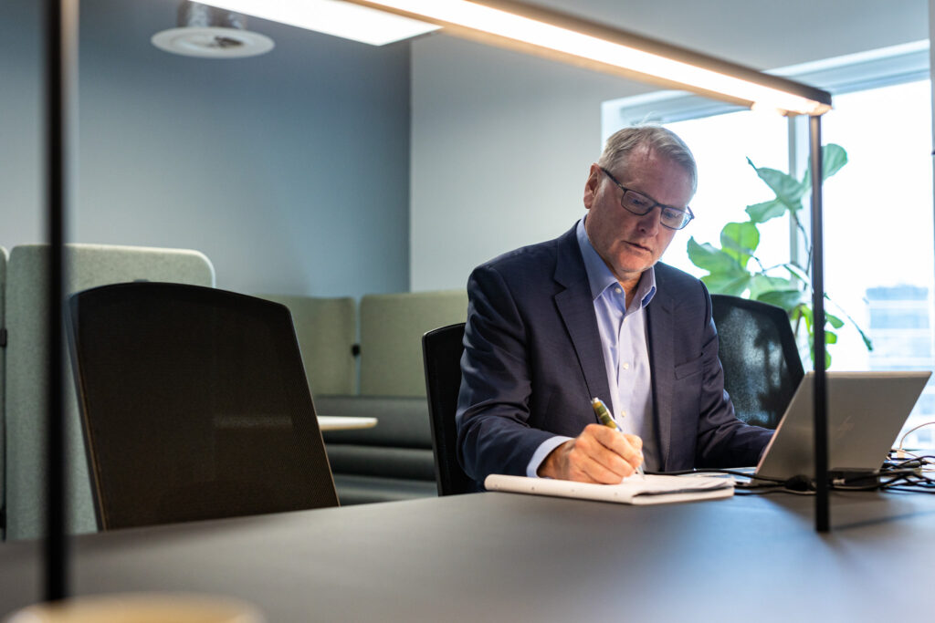 A man in a suit working at a desk in a modern open plan office space.